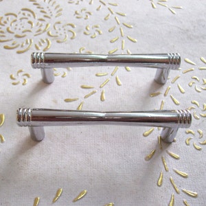 May include: Two silver cabinet door pulls with a simple, straight design. The pulls have a slightly textured finish.