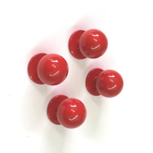 May include: Four red plastic knobs with a round shape and a flat base. The knobs are arranged in a diamond shape on a white background.