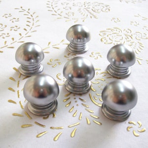 Könnte beinhalten: Sechs silberne Schrankknöpfe mit runder, glatter Oberseite und geriffeltem Sockel.