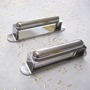 May include: Two chrome guitar pickup covers. The covers are rectangular with a rounded edge and a cylindrical center section.