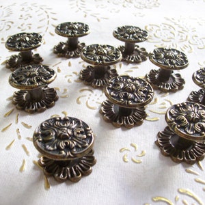 May include: A set of antique bronze cabinet knobs. Each knob has a detailed floral design on a round face, mounted on a decorative base. The knobs are arranged on a white surface with a subtle pattern.