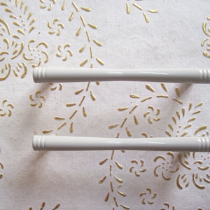 May include: Two white ceramic drawer pulls with a ribbed design. The pulls are on a white background with a gold floral pattern.