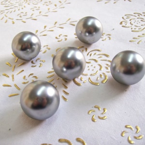 Può includere: Cinque ornamenti rotondi color argento su uno sfondo bianco con un motivo floreale dorato.