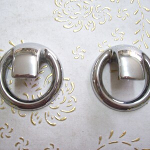 Op de afbeelding: Twee zilveren ringvormige ladegrepen met elk een vierkant handvat.