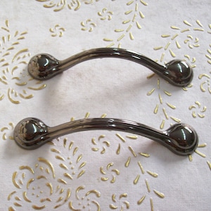 May include: Two black metal cabinet door pulls with a curved design. The pulls have a shiny finish.