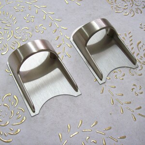 May include: Two silver metal wall mounted towel holders. The holders are shaped like a curved arch with a flat base.
