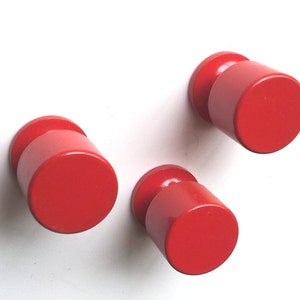 Könnte beinhalten: Drei runde rote Schrankknöpfe mit zylindrischer Basis.