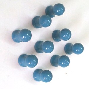 Peut inclure: Dix boutons en céramique bleus avec un dessus arrondi et une petite base. Les boutons sont disposés en cercle sur un fond blanc.