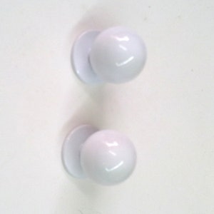 Peut inclure: Deux boutons ronds en plastique blanc avec une base plate. Les boutons sont lisses et ont une finition brillante.