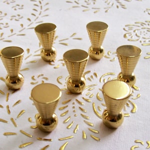 May include: Seven gold-toned metal knobs with a round base and a cone-shaped top. The knobs have a textured surface.
