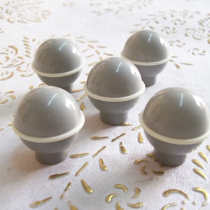 Puede incluir: Cinco pomos redondos para armarios de color gris y blanco con un acabado liso y brillante.