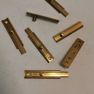 Puede incluir: Un juego de ocho pestillos de puerta de metal dorado. Los pestillos son de diferentes tamaños y formas, pero todos tienen un diseño similar. Todos están hechos de un metal liso y brillante.