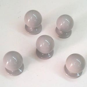 May include: Five gray ceramic cabinet knobs with a round shape and a slightly raised base.