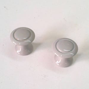 Puede incluir: Dos pomos de armario pequeños, redondos y grises con un borde elevado alrededor del borde.