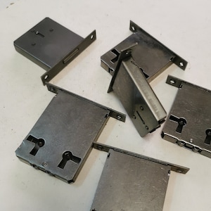 Peut inclure: Six plaques de serrure de porte argentées avec le texte "BREV CAS" dessus. Les plaques sont disposées de manière aléatoire sur une surface blanche.