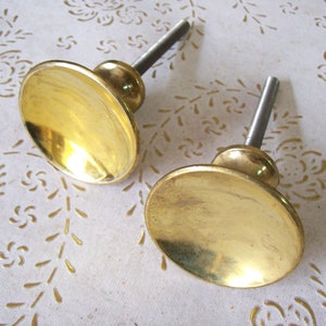 May include: Two brass cabinet knobs with a round, slightly domed shape and a shiny finish. The knobs have a threaded metal stem for attaching to a cabinet door.