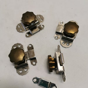 Puede incluir: Cuatro cierres de puerta de armario de metal plateado con un pomo de color dorado. Cada cierre tiene un borde decorativo y cuatro pequeños agujeros para el montaje.