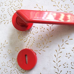 Może przedstawiać: Zestaw dwóch okrągłych, czerwonych gałek do drzwi z małym otworem w środku.