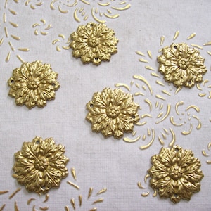 Può includere: Sei decorazioni metalliche dorate con un motivo floreale. Le decorazioni sono disposte in un cerchio su uno sfondo bianco.