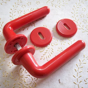 May include: Set of bright red door handles and matching keyhole covers. The handles have a curved design and are made of a glossy material. The keyhole covers are round with a slot for the key. Hardware for home improvement.