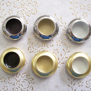 Peut inclure: Six poignées de tiroir rondes en métal avec différentes finitions. Les poignées sont chromées, dorées et blanches.