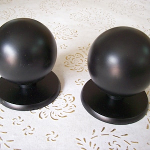 Peut inclure: Deux boutons de porte ronds noirs avec une finition lisse et brillante. Chaque bouton est monté sur une base ronde.
