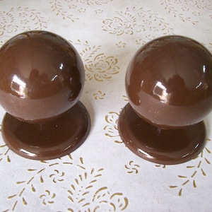 Puede incluir: Dos remates de cerámica marrón con un acabado brillante. Los remates son redondos y tienen una superficie lisa.