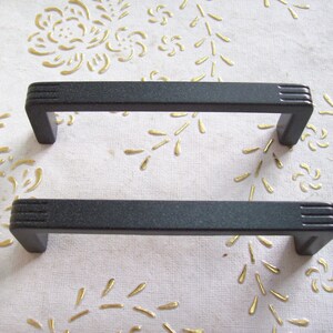 Peut inclure: Deux poignées de porte de placard noires avec une finition texturée. Les poignées sont rectangulaires avec des bords arrondis et ont une légère courbe au milieu.