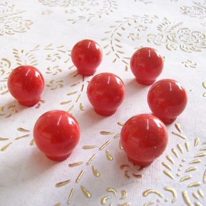 以下が含まれることがあります： わずかにテクスチャ加工された表面を持つ、赤い丸いガラスのノブが7つあります