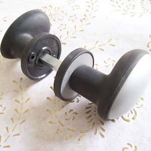 May include: A black door knob with a silver metal rod and a gray plastic handle.