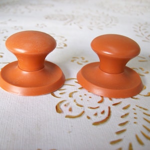 May include: Two orange plastic cabinet knobs with a round base and a raised round top.