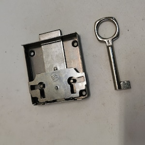 May include: A silver metal lock with a keyhole and a silver key. The lock has the word "SIS" printed on it.