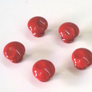 May include: Five red ceramic knobs with a smooth, rounded surface. The knobs have a small indentation in the centre.