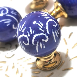 May include: Close-up of several blue and white ceramic cabinet knobs. Each knob has a spherical shape with a white, abstract design. The knobs are mounted on gold-colored metal bases, suggesting a decorative hardware theme.