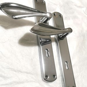 Könnte beinhalten: Ein Set aus drei Keramikbechern mit gesprenkelter, matter Oberfläche. Die Becher sind in Creme-, Hellgrau- und Dunkelgrautönen gehalten. Jeder Becher hat ein schlichtes, minimalistisches Design und einen abgerundeten Henkel. Für Kaffee oder Tee.