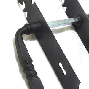 Puede incluir: Primer plano de un juego de manijas de puerta negro y ornamentado. El mango presenta un diseño retorcido y está unido a una placa rectangular con bordes decorativos. Un ojo de cerradura es visible en la placa. El herraje es de metal.