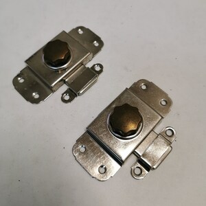 Op de afbeelding: Twee zilverkleurige metalen kastdeurgrepen met een bruine knop. Elke greep heeft een klein metalen scharnier.