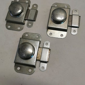 Può includere: Tre chiavistelli in metallo color argento con pomello e meccanismo scorrevole. Ogni chiavistello ha una base rettangolare con quattro fori per viti e un piccolo fermo rettangolare. I pomelli sono rotondi e leggermente bombati.