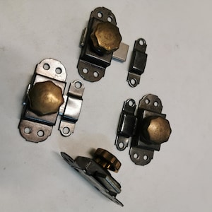 May include: Four antique-style metal cabinet door catches with brass knobs. The catches are black and silver in color and have a decorative design.