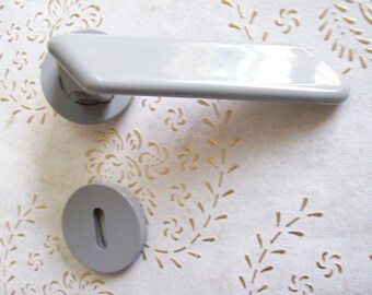 May include: A white door handle with a round base and a rectangular lever. The handle is mounted on a white wall with a floral pattern.