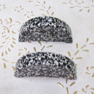 Può includere: Due pomelli per mobili in ceramica macchiati di bianco e nero. I pomelli hanno la forma di semicerchi.