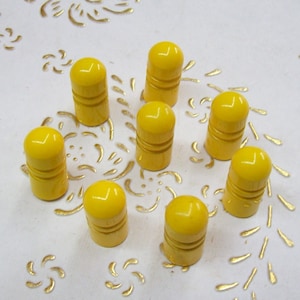 Può includere: Nove tappi per bottiglie gialli su una superficie bianca con un motivo floreale dorato.