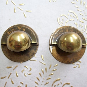 May include: Two brass cabinet knobs with a round, slightly domed top and a half-circle design around the base.