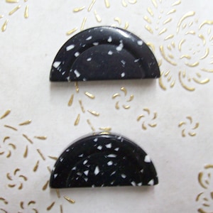 May include: Two black and white speckled half-circle shaped buttons. The buttons are made of a hard plastic material.