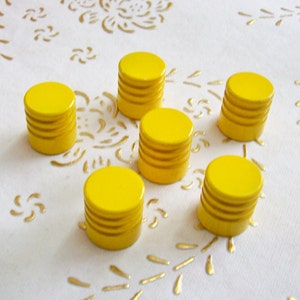 May include: Six yellow wooden knobs with a grooved design. The knobs are arranged in a semi-circle on a white surface with a gold floral pattern.