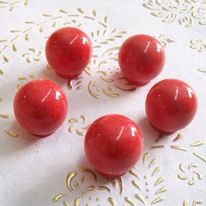 May include: Five red, round, smooth, ceramic knobs with a slightly textured surface.