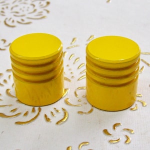 Puede incluir: Dos pomos redondos amarillos para armario con tres líneas elevadas alrededor del centro.