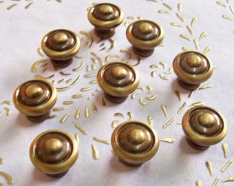 May include: Ten antique brass cabinet knobs with a circular design. The knobs have a raised centre and a slightly rounded edge.