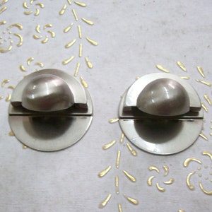 May include: Two silver-toned door knobs with a rounded top and a flat base. The knobs are separated by a small gap.