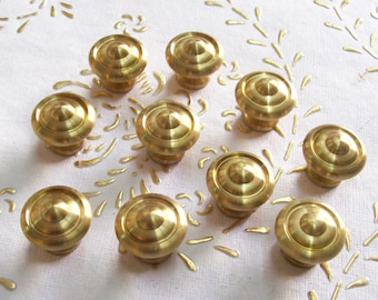 May include: Ten gold-toned metal cabinet knobs with a rounded, domed top. The knobs are arranged in a circular pattern on a white surface.